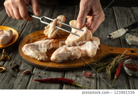 Hands carefully sort through raw chicken wings on a wooden cutting board. A knife, herbs and garlic are laid out nearby, indicating that a fragrant dish is being prepared Hands carefully sort through raw chicken wings on a wooden cutting board. A knife, herbs and garlic are laid out nearby, indicating that a fragrant dish is being prepared 123981556