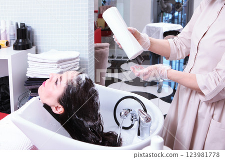Woman washes her hair in beauty salon. Strengthening and treatment of hair. Concept of spa services. Woman washes her hair in beauty salon. Strengthening and treatment of hair. Concept of spa services. 123981778