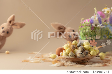 Easter eggs, feathers, spring flowers, and toy bunny on a beige background. Easter eggs, feathers, spring flowers, and toy bunny on a beige background. 123981781
