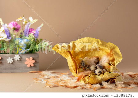 Crepe paper nest with easter eggs, feathers, and spring flowers on a beige background. 123981783