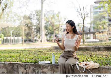 Sustainable lifestyle. Woman engaging with smartphone outdoors in a park setting. 123981848