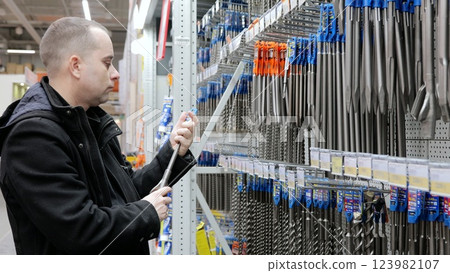 Construction worker comparing drill bit options in hardware store, selecting precise tool matching specific needs for professional renovation project 123982107