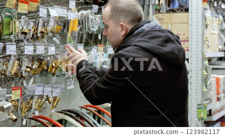 Skilled plumber examining plumbing fixtures in hardware store, comparing faucets and connectors for upcoming professional installation project 123982117