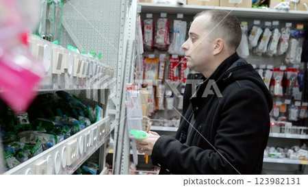 Experienced electrician comparing light switch models in hardware store, selecting precise electrical components for professional installation and home improvement needs 123982131