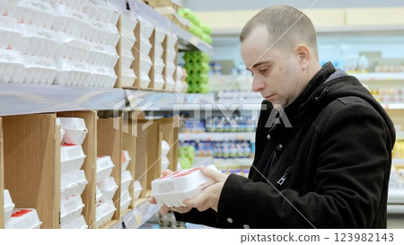 Focused mature male selecting free range eggs, examining packaging details while grocery shopping in supermarket aisle Focused mature male selecting free range eggs, examining packaging details while grocery shopping in supermarket aisle 123982143