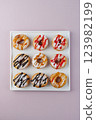 donuts with powdered sugar and various toppings on a white plate on a pale purple background. Top view . Copy space 123982199