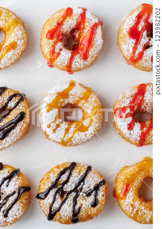 A group of donuts with powdered sugar and various toppings on a white plate close-up. Top view A group of donuts with powdered sugar and various toppings on a white plate close-up. Top view 123982202