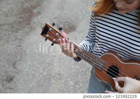 Girl Strums With Ukulele Musical Instrument Near A Tree In The Mountains 123982229