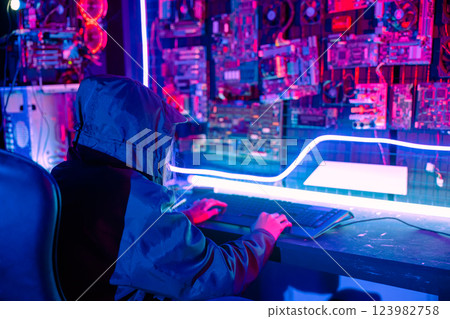 Woman hacker. Asian woman wearing hood is typing keyboard for coding hacking programming system. room is dimly lit. possibly typing or browsing internet, Hacker in neon light, Female gamer play game 123982758