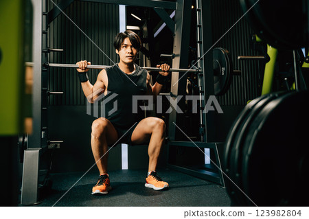 Asian muscular man guy performing a squat exercise legs heavy weights with a barbell in gym, men doing lifting barbell work out at fitness gym, sport workout healthy lifestyle concept Asian muscular man guy performing a squat exercise legs heavy weights with a barbell in gym, men doing lifting barbell work out at fitness gym, sport workout healthy lifestyle concept 123982804