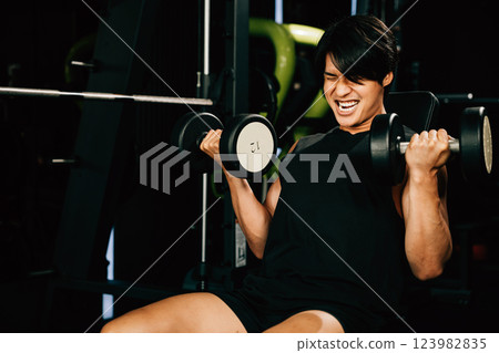 Asian man muscular lifting dumbbell on bench in fitness gym, Happy young men doing strength training press exercise with dumbbells in a gym, workout weight training healthy lifestyle concept 123982835