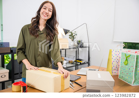 Asian young woman packing box with tape before shipping to customer at home office, businesswoman sealing packages with tape at desk, startup small business on websites and social media 123982872