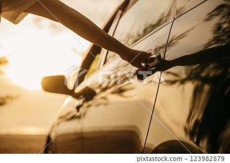 Close up young woman hand opening opening the door of a car at sunset. Hand holding door hand to open to get into driver seat. Travel road trip concept 123982879
