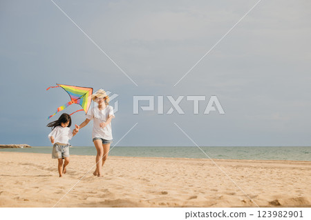 Asian family is flying a kite high in the sky while running on the beach. Happy parents mother with their child playing with kite, family is enjoying their time together, summer day Asian family is flying a kite high in the sky while running on the beach. Happy parents mother with their child playing with kite, family is enjoying their time together, summer day 123982901