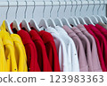 A vibrant collection of jackets hangs neatly on hangers, showcasing a spectrum of colors including yellow, red, pink, and white, set against a simple backdrop. 123983363