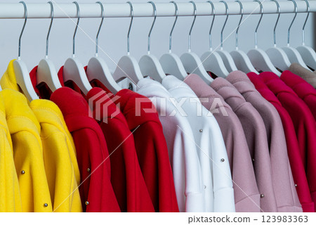 A vibrant collection of jackets hangs neatly on hangers, showcasing a spectrum of colors including yellow, red, pink, and white, set against a simple backdrop. A vibrant collection of jackets hangs neatly on hangers, showcasing a spectrum of colors including yellow, red, pink, and white, set against a simple backdrop. 123983363
