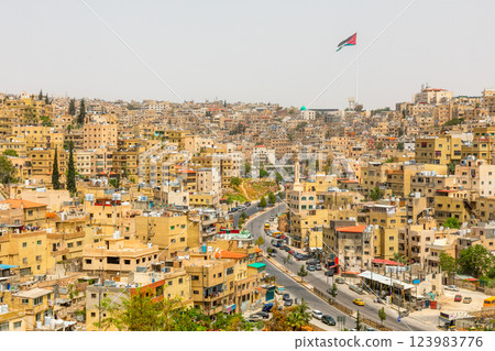Lots of residential houses densily scattered on the hills in the downtown of Amman city with national flag waving on the wind, Kingdom of Jordan 123983776