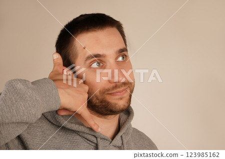 A playful man mimics a phone call by holding his hand near his ear. His cheerful look adds personality to the scene. The image highlights a casual and lighthearted vibe. A playful man mimics a phone call by holding his hand near his ear. His cheerful look adds personality to the scene. The image highlights a casual and lighthearted vibe. 123985162