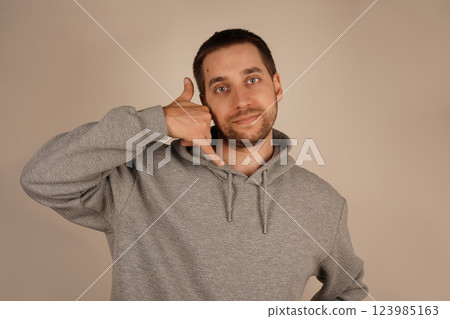 His cheerful look adds personality to the scene. The image highlights a casual and lighthearted vibe. A playful man mimics a phone call by holding his hand near his ear. His cheerful look adds personality to the scene. The image highlights a casual and lighthearted vibe. A playful man mimics a phone call by holding his hand near his ear. 123985163
