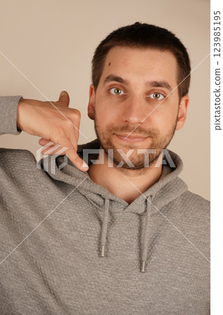 A playful man mimics a phone call by holding his hand near his ear. His cheerful look adds personality to the scene. The image highlights a casual and lighthearted vibe. A playful man mimics a phone call by holding his hand near his ear. His cheerful look adds personality to the scene. The image highlights a casual and lighthearted vibe. 123985195