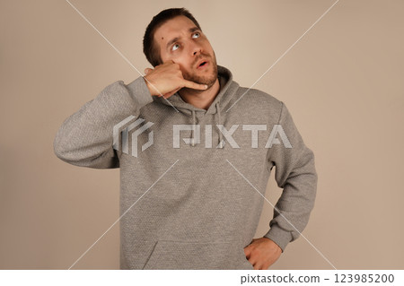 The man positions his hand like a phone near his ear, pretending to make a call. His relaxed demeanor suggests a fun and informal moment. The gesture conveys creativity and humor. The man positions his hand like a phone near his ear, pretending to make a call. His relaxed demeanor suggests a fun and informal moment. The gesture conveys creativity and humor. 123985200