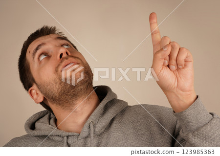 The gesture draws attention and conveys urgency. With a single raised finger, the man points upward to underscore a significant idea. His expressive face supports the gesture's intent. The gesture draws attention and conveys urgency. With a single raised finger, the man points upward to underscore a significant idea. His expressive face supports the gesture's intent. 123985363