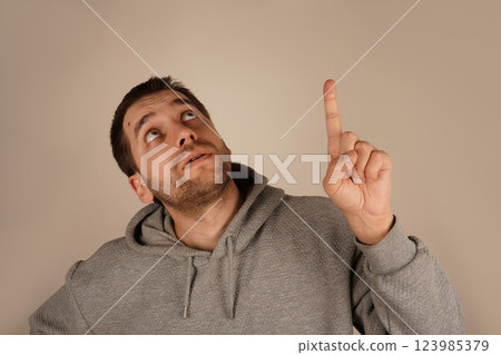 His expressive face supports the gesture's intent. The gesture draws attention and conveys urgency. With a single raised finger, the man points upward to underscore a significant idea. His expressive face supports the gesture's intent. The gesture draws attention and conveys urgency. With a single raised finger, the man points upward to underscore a significant idea. 123985379
