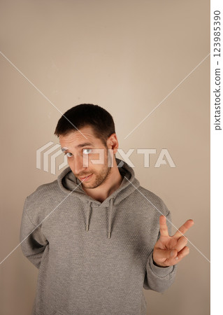 The boy in a grey hoodie flashes a peace sign, holding up his fingers in a "V" shape. His relaxed pose symbolizes calm and goodwill. The gesture speaks of peace and togetherness. 123985390