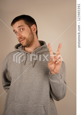 His relaxed pose symbolizes calm and goodwill. The gesture speaks of peace and togetherness. The boy in a grey hoodie flashes a peace sign, holding up his fingers in a "V" shape. His relaxed pose symbolizes calm and goodwill. The gesture speaks of peace and togetherness. The boy in a grey hoodie flashes a peace sign, holding up his fingers in a "V" shape. 123985391