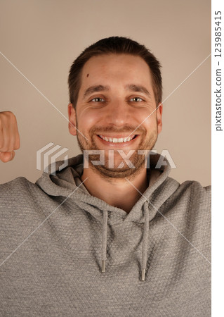 The smile makes the gesture feel friendly and motivating. With a cheerful smile, the young man flexes his arm, highlighting his strong bicep. His pose reflects both physical strength and confidence. The smile makes the gesture feel friendly and motivating. With a cheerful smile, the young man flexes his arm, highlighting his strong bicep. His pose reflects both physical strength and confidence. 123985415