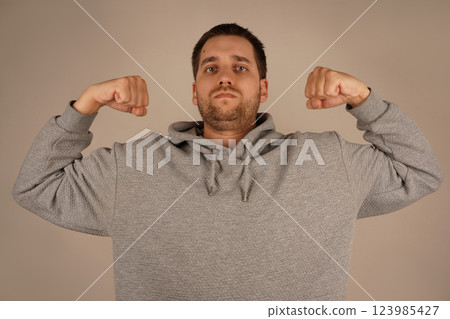 This gesture radiates power and pride in his physique. Flexing both arms, the man demonstrates his biceps and clenched fists. His pose emphasizes his physical strength and confidence. 123985427