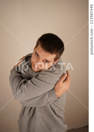 His gesture expresses self-love and warmth. The scene feels intimate and comforting. A young man with a light beard gently hugs himself with both arms, creating a cozy and emotional vibe. His gesture expresses self-love and warmth. The scene feels intimate and comforting. A young man with a light beard gently hugs himself with both arms, creating a cozy and emotional vibe. 123985440