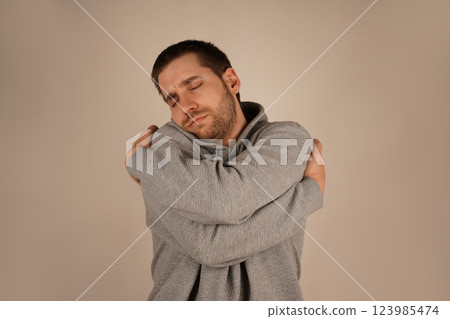 His embrace highlights emotional comfort and self-affection. It s a tender, cozy moment. With a light beard, the young man holds himself close, offering a sense of warmth and serenity. His embrace highlights emotional comfort and self-affection. It s a tender, cozy moment. With a light beard, the young man holds himself close, offering a sense of warmth and serenity. 123985474