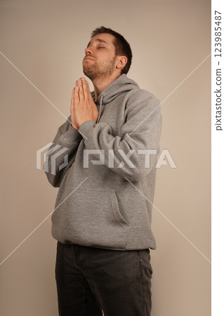 The young man, dressed in athletic wear, places his palms together in a prayer gesture. His expression is calm, creating a sense of earnest prayer or quiet reflection. It s a moment of connection. The young man, dressed in athletic wear, places his palms together in a prayer gesture. His expression is calm, creating a sense of earnest prayer or quiet reflection. It s a moment of connection. 123985487