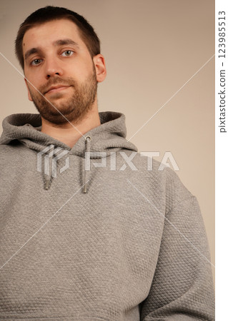 His face shows a relaxed demeanor, giving off a casual vibe. The side view of a man in a grey hoodie highlights his short dark hair and light stubble. 123985513