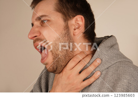 A man grips his throat with his hand, mouth wide open as if he s choking or coughing. The discomfort on his face shows the urgency of the moment, as he struggles with breathing or a strong cough. 123985603