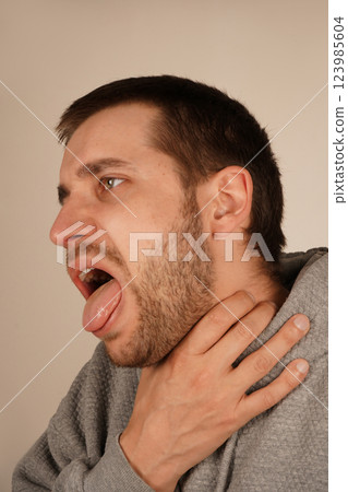 The discomfort on his face shows the urgency of the moment, as he struggles with breathing or a strong cough. A man grips his throat with his hand, mouth wide open as if he s choking or coughing. 123985604