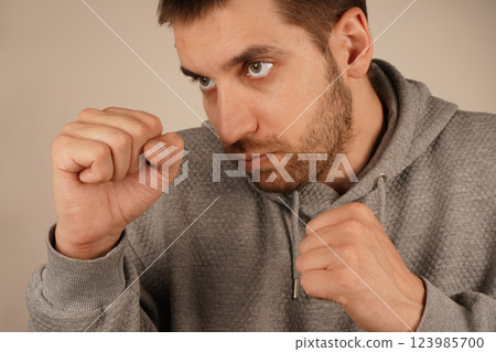 His pose resembles that of a boxer, radiating energy and confidence. The mood is dynamic and intense. Wearing a sports hoodie, the man stands with fists clenched, prepared for action. His pose resembles that of a boxer, radiating energy and confidence. The mood is dynamic and intense. Wearing a sports hoodie, the man stands with fists clenched, prepared for action. 123985700