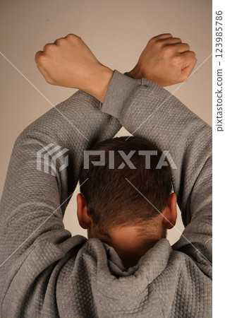 A rear view of a man with arms crossed above his head, forming clenched fists. His posture exudes confidence and strength. The scene highlights power and determination. A rear view of a man with arms crossed above his head, forming clenched fists. His posture exudes confidence and strength. The scene highlights power and determination. 123985786