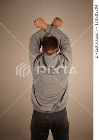 His posture exudes confidence and strength. The scene highlights power and determination. A rear view of a man with arms crossed above his head, forming clenched fists. 123985804