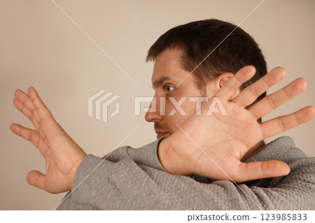 With arms crossed and fingers spread wide, a man creates a gesture of restriction or shielding. His open palms emphasize a defensive and assertive position. The image exudes caution and strength. 123985833