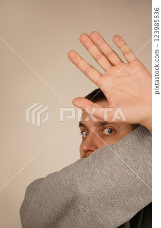 With arms crossed and fingers spread wide, a man creates a gesture of restriction or shielding. His open palms emphasize a defensive and assertive position. The image exudes caution and strength. 123985836