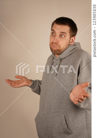 With hands extended outward, a man shrugs, appearing confused. The open palms symbolize his lack of understanding about the situation. His body language reflects uncertainty and wonder. With hands extended outward, a man shrugs, appearing confused. The open palms symbolize his lack of understanding about the situation. His body language reflects uncertainty and wonder. 123985838