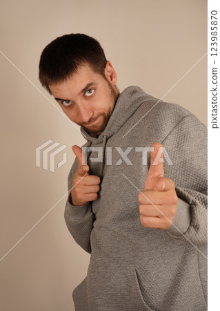 The pose highlights confidence and direction. In gray athletic wear, the man uses his index fingers to point in one direction. This action suggests clarity and decisiveness. The pose highlights confidence and direction. In gray athletic wear, the man uses his index fingers to point in one direction. This action suggests clarity and decisiveness. 123985870