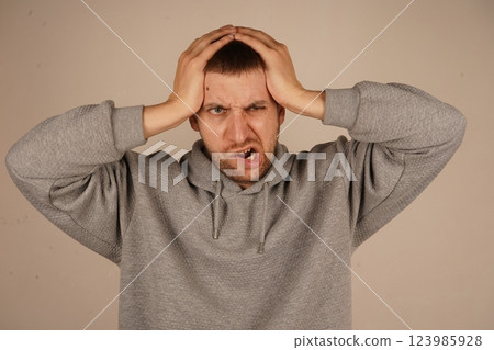 With both hands placed firmly on his head, the man shows signs of stress or a headache. His posture and expression reveal strain. This shot emphasizes the physical manifestation of mental discomfort. With both hands placed firmly on his head, the man shows signs of stress or a headache. His posture and expression reveal strain. This shot emphasizes the physical manifestation of mental discomfort. 123985928