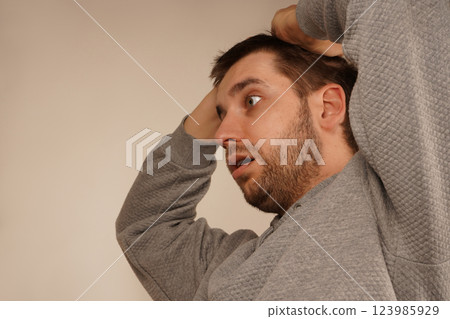 His posture and expression reveal strain. This shot emphasizes the physical manifestation of mental discomfort. With both hands placed firmly on his head, the man shows signs of stress or a headache. His posture and expression reveal strain. This shot emphasizes the physical manifestation of mental discomfort. With both hands placed firmly on his head, the man shows signs of stress or a headache. 123985929