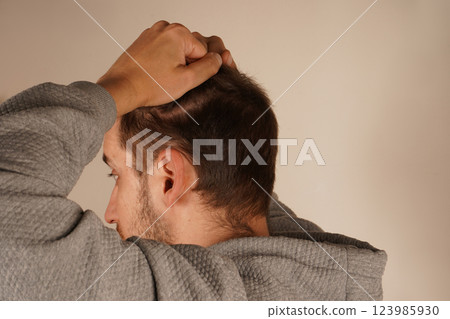 With both hands placed firmly on his head, the man shows signs of stress or a headache. His posture and expression reveal strain. This shot emphasizes the physical manifestation of mental discomfort. With both hands placed firmly on his head, the man shows signs of stress or a headache. His posture and expression reveal strain. This shot emphasizes the physical manifestation of mental discomfort. 123985930