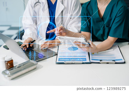 Medical team having a meeting with doctors in white lab coats and surgical scrubs seated at a table 123989275