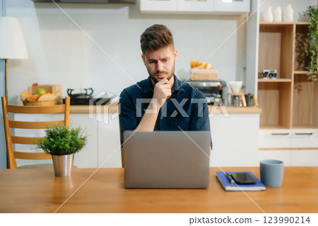 Businessman using laptop while sitting at home. Young man sitting in kitchen and working Businessman using laptop while sitting at home. Young man sitting in kitchen and working 123990214