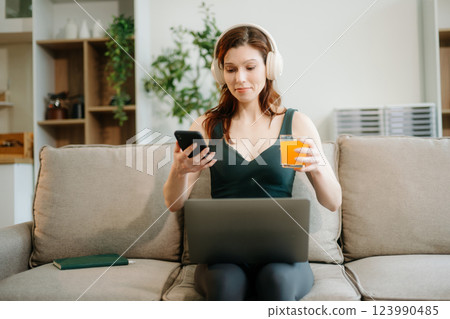 Happy woman with headphones using a laptop in a cozy living room with food and drink. Perfect for themes Happy woman with headphones using a laptop in a cozy living room with food and drink. Perfect for themes 123990485